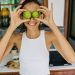 Smiling young woman playfully holding limes over her eyes in a bright kitchen, capturing a fun and positive moment.