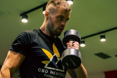 Muscular man exercising with a dumbbell in a modern gym setting, emphasizing strength and fitness.